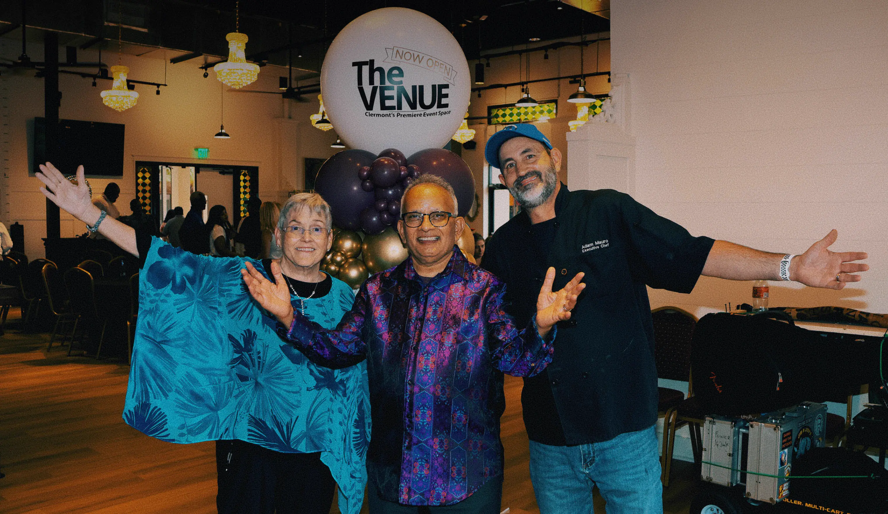 Hosts and catering team with arms open celebrating the grand opening of The Venue Clermont inside the main venue with festive balloon display